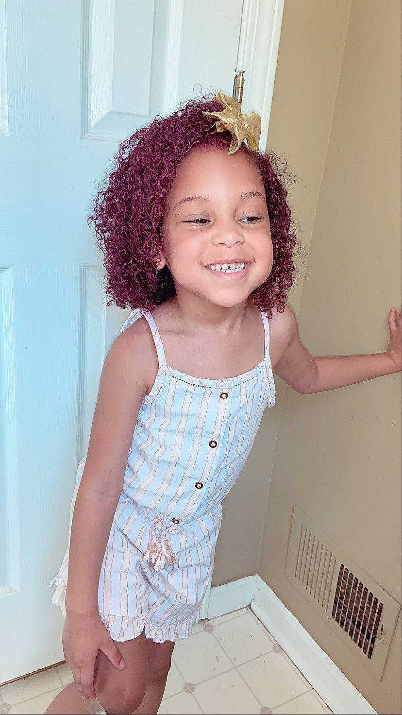 Camilla is registered to the contest to win money with this photo: baby_toddler_clothing, chin, clothing, face, fashion_design, hair, happy, headgear, iris, joy, long_hair, neck, person, pink, purple, shoulder, skin, sleeve, smile, thigh