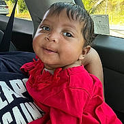 Hope is registered to the contest to win money with this photo: baby, child, red_clothing, car_interior, seatbelt, person, portrait, cute, smiling, window, daylight, nature_outside, holding, happy, face, infant, casual, travel, young, human