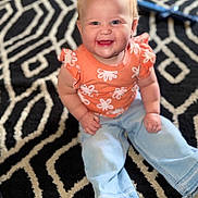 Everleigh joined the competition — help win amazing prizes! baby, child, smiling, happy, sitting, jeans, orange_top, patterned_rug, indoor, cute, blonde_hair, blue_eyes, barefoot, portrait, casual_clothing, young_child, infant, person, home, floor