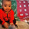 Kai is registered to the contest to win money with this photo: baby, child, red_jacket, water_bottle, milestone_blanket, numbers, helmet_marker, couch, cozy, smile, curious, indoor, cute, portrait, sitting, person, clothing, home, celebration, happy