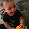 Kai joined the competition — help win amazing prizes! baby, child, toddler, smiling, toy, orange, black_clothing, couch, indoor, person, happy, curly_hair, sitting, playful, small_hands, closeup, casual, home, infant, cute