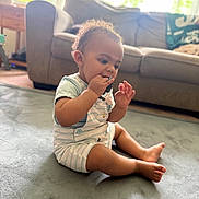 Kai joined the competition — help win amazing prizes! baby, child, toddler, indoor, carpet, couch, toy, curly_hair, light, window, living_room, sitting, chewing, clothing, shorts, striped, floor, person, cute, young