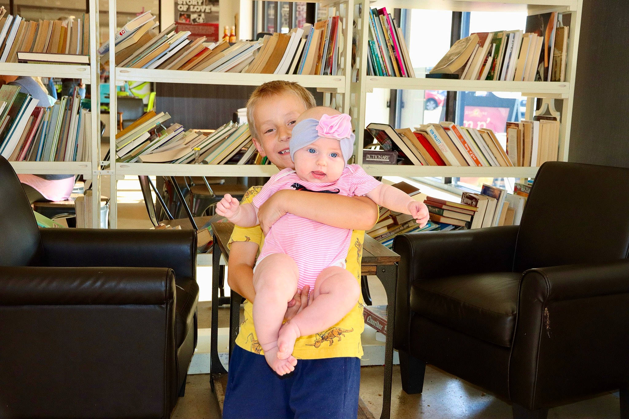 Megan is registered to the contest to win money with this photo: book, bookcase, chair, comfort, couch, flooring, fun, furniture, headwear, joy, knee, lap, living_room, person, publication, room, shelf, shelving, sitting, smile