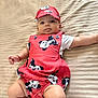 baby, infant, panda_print, cap, red_outfit, bedspread, striped_bed, lying_down, cute, child, adorable, skin, arm, leg, clothing, face, headwear, bracelet, indoors, portrait