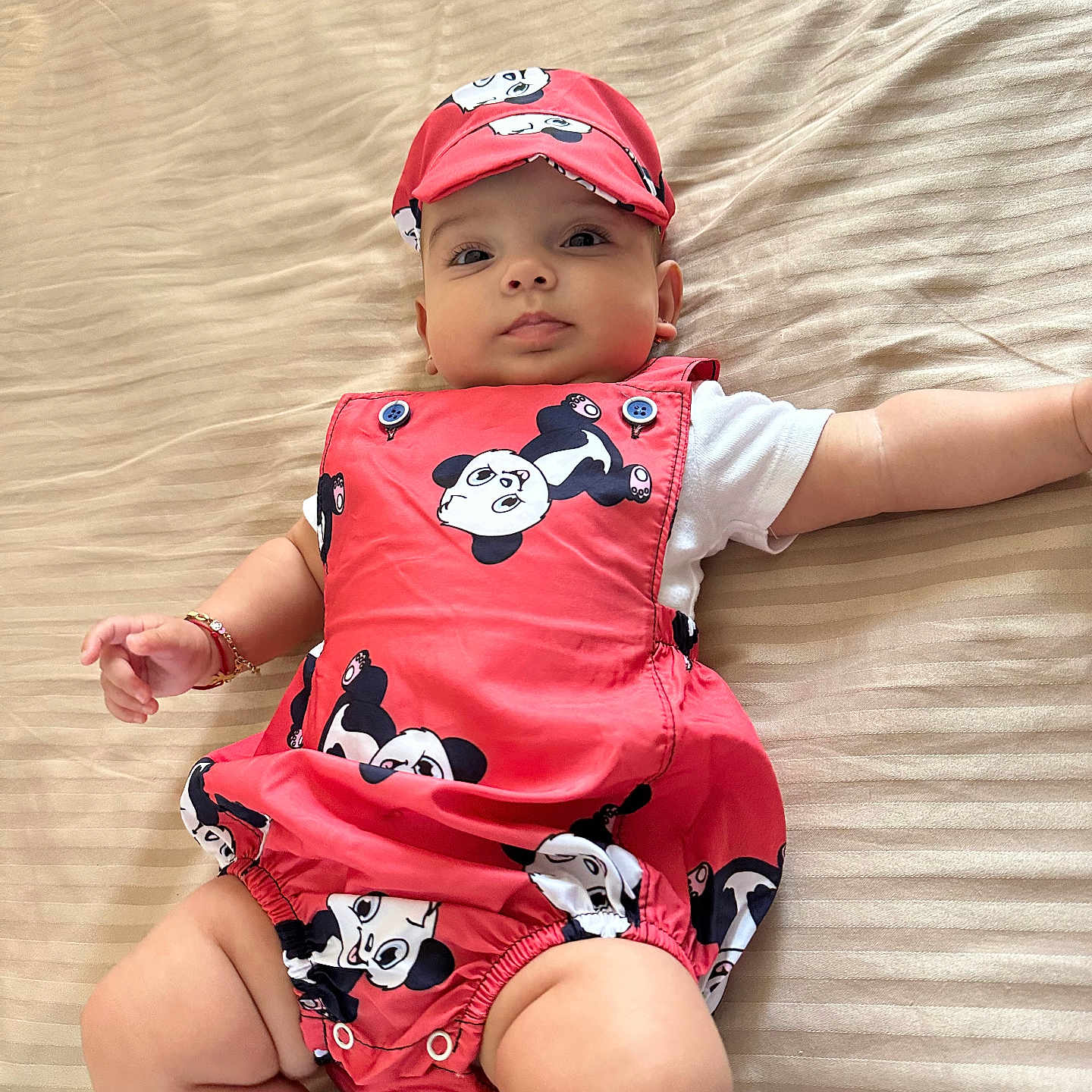 Leea participe au concours pour gagner de l'argent avec cette photo : adorable, arm, baby, bedspread, bracelet, cap, child, clothing, cute, face, headwear, indoors, infant, leg, lying_down, panda_print, portrait, red_outfit, skin, striped_bed