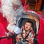toddler, child, stroller, crying, santa_claus, red_clothing, white_beard, glasses, gloves, outdoor, winter_clothing, expression, face, person, holiday, festive, hat, patterned_pants, comfort, emotion