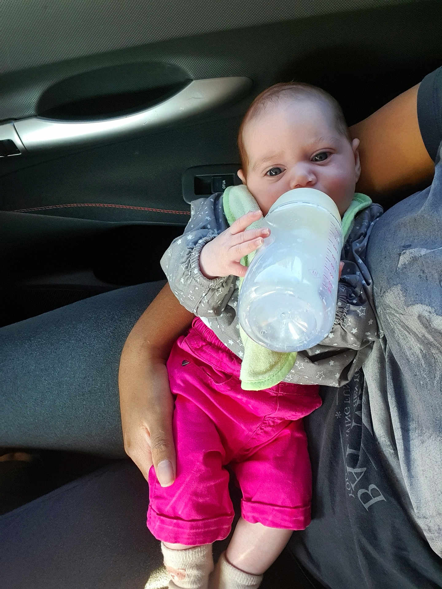 Cataleya participe au concours pour gagner de l'argent avec cette photo : baby, bottle, feeding, infant, car_interior, person, hand, clothing, pink_pants, gray_shirt, seat, door_handle, window_control, socks, holding, closeup, cute, child, casual, indoor