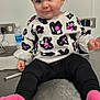 baby, black_pants, child, clothing, cute, electrical_outlet, exit_sign, expression, face, hair, indoor, metal_table, person, pigtails, pink_socks, playful, sitting, smiling, sweater, water_bottle