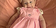 Sophia is registered to the contest to win money with this photo: baby, child, pink_dress, headband, bow, smile, cushion, blanket, infant, cute, portrait, lying_down, happy, indoors, soft_lighting, skin, person, small_hands, clothing, face