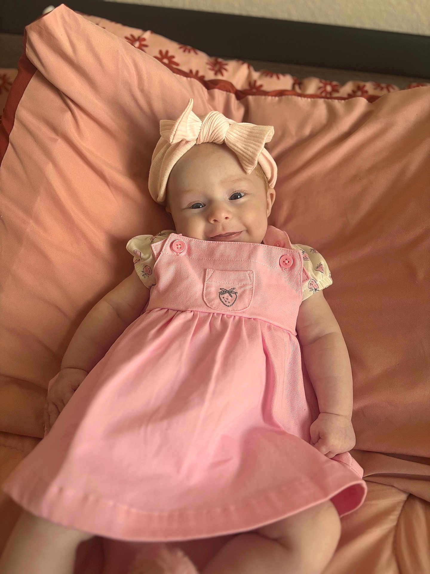 Sophia is registered to the contest to win money with this photo: baby, child, pink_dress, headband, bow, smile, cushion, blanket, infant, cute, portrait, lying_down, happy, indoors, soft_lighting, skin, person, small_hands, clothing, face