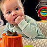 baby, infant, child, face, hand, toy, activity_seat, indoor, cables, fan, playtime, curious, bright_eyes, clothing, closeup, furniture, colorful, plastic, expression, cute