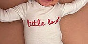 Naya a rejoint le concours — aidez-le/la à gagner de superbes lots ! baby, smiling, infant, onesie, clothing, lying_down, happy, cute, child, face, skin, head, arms, legs, text_on_clothing, indoor, soft_surface, love, red_text, closeup