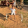 child, boy, swing, outdoor, sunlight, dirt, wooden_swing, rope, smiling, casual_clothing, shorts, sandals, deck, plant_pots, fence, nature, daylight, happy, play, recreation