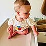 Jules participe au concours pour gagner de l'argent avec cette photo : baby, child, tshirt, balloons, changing_table, drawer, hand, foot, skin, room, furniture, curious, indoors, clothing, person, head, hair, babycare, soft, white