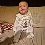 Amelia is registered to the contest to win money with this photo: baby, child, infant, smiling, sitting, christmas_outfit, pajamas, couch, pillow, fabric, indoor, happy, young_child, cute, holiday, festive, clothing, portrait, person, cozy