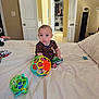 toddler, child, bed, toy, ball, snack_bag, room, closet, door, blanket, pajamas, floor, furniture, indoor, curious, sitting, face, expression, playtime, home