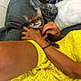 cat, person, hand, yellow_dress, blanket, couch, grey_blanket, feline, pet, relaxing, comfort, indoor, resting, animal, spotted_cat, striped_cat, content, affection, close_up, domestic