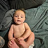 baby, infant, diaper, barefoot, holding_feet, blanket, tattoo, adult_leg, blue_blanket, playful, indoor, person, child, cute, skin, smiling, lying_down, casual, family, relaxed
