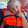 child, life_jacket, orange, blue_eyes, blonde_hair, braids, playful, smiling, sitting, outdoor, summer, boat, safety, person, portrait, cute, casual_clothing, bright_colors, fun, relaxed