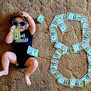 Raiden joined the competition — help win amazing prizes! baby, child, infant, portrait, sunglasses, cowboy_hat, hat, money, dollar_bills, cash, dollar_sign, carpet, indoor, sitting, lying_down, black_clothing, fashion, playful, funny, photography