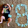 baby, child, infant, portrait, sunglasses, cowboy_hat, hat, money, dollar_bills, cash, dollar_sign, carpet, indoor, sitting, lying_down, black_clothing, fashion, playful, funny, photography