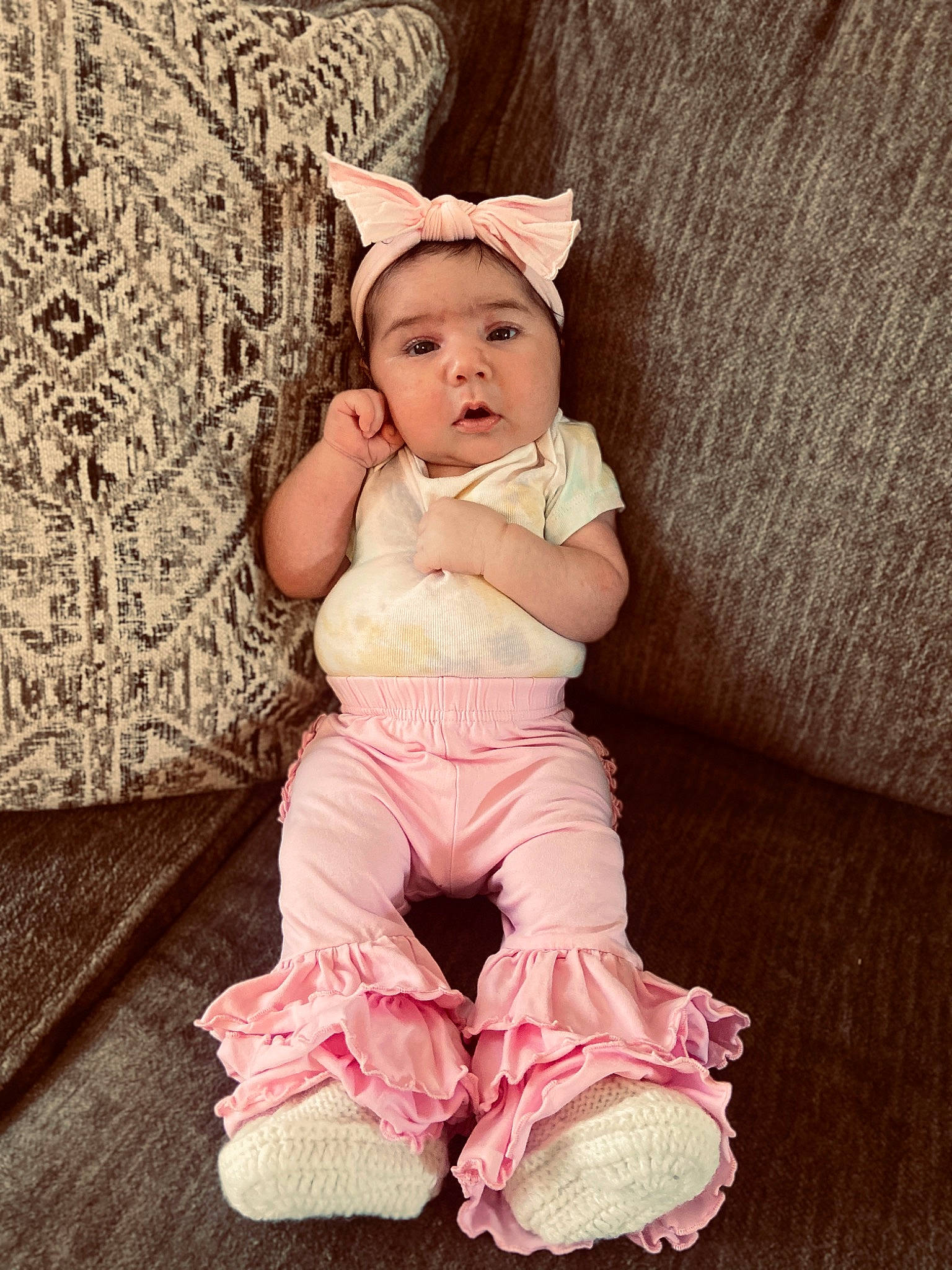 Selena is registered to the contest to win money with this photo: baby, baby_toddler_clothing, cheek, comfort, face, facial_expression, flash_photography, flooring, foot, happy, headwear, linens, magenta, pattern, person, pink, sitting, skin, sleeve, textile