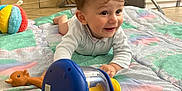 Cyriak participe au concours pour gagner de l'argent avec cette photo : baby, child, toy, rattle, quilt, colorful, smiling, indoor, floor, high_chair, giraffe_toy, striped_book, play, crawling, happy, clothing, person, head, face, furniture