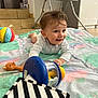 baby, child, toy, rattle, quilt, colorful, smiling, indoor, floor, high_chair, giraffe_toy, striped_book, play, crawling, happy, clothing, person, head, face, furniture