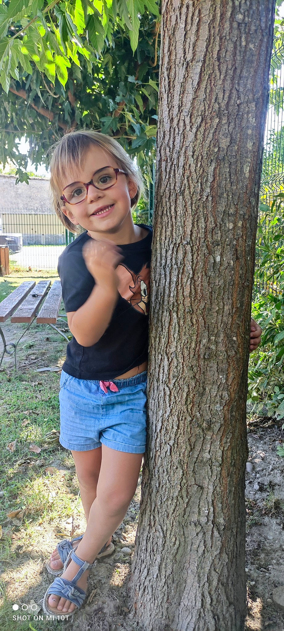 Mia a rejoint le concours — aidez-le/la à gagner de superbes lots ! eyewear, facial_expression, glasses, grass, hairstyle, happy, human_body, jean_short, joy, people_in_nature, person, plant, shorts, shoulder, smile, standing, t_shirt, tree, trunk, vision_care
