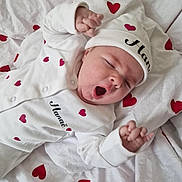 Hanaë a rejoint le concours — aidez-le/la à gagner de superbes lots ! baby, infant, yawning, sleepy, white_clothing, red_hearts, hat, blanket, cute, newborn, small_hands, lying_down, soft_fabric, cozy, child, adorable, peaceful, portrait, resting, face