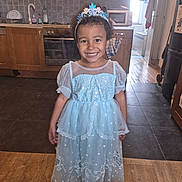 Maëlys a rejoint le concours — aidez-le/la à gagner de superbes lots ! child, smiling, dress, princess, tiara, kitchen, floor, cabinet, microwave, oven, happy, curly_hair, barefoot, tile_floor, wood_floor, appliance, indoor, young_girl, portrait, home