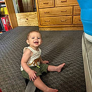 Wylder is registered to the contest to win money with this photo: baby, carpet, casual, child, clothing, cute, floor, footwear, furniture, happy, home, indoor, person, room, sandal, shorts, sitting, smiling, tank_top, wooden_dresser