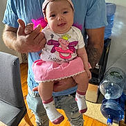 Jessenia joined the competition — help win amazing prizes! baby, child, infant, pink_skirt, headband, socks, adult, holding, indoor, water_dispenser, wooden_floor, blue_shirt, ripped_jeans, happy, playful, tongue_out, person, casual_clothing, home, furniture