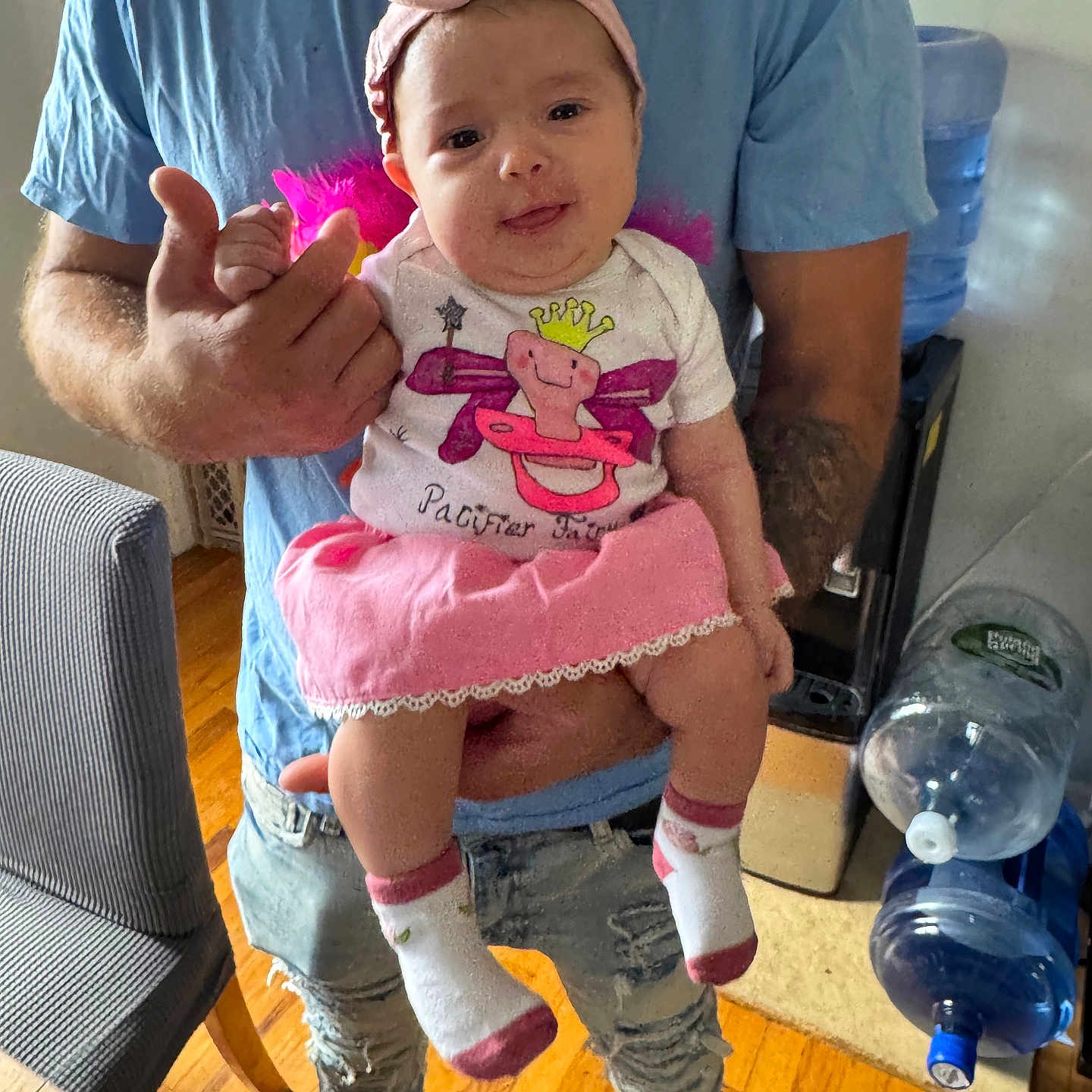 Jessenia joined the competition — help win amazing prizes! adult, baby, blue_shirt, casual_clothing, child, furniture, happy, headband, holding, home, indoor, infant, person, pink_skirt, playful, ripped_jeans, socks, tongue_out, water_dispenser, wooden_floor