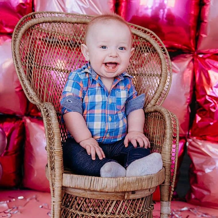 Ryler joined the competition — help win amazing prizes! baby, background, balloons, celebration, child, colorful, cute, festive, happy, indoor, infant, joyful, metallic, pink, plaid_shirt, portrait, silver, smiling, socks, wicker_chair