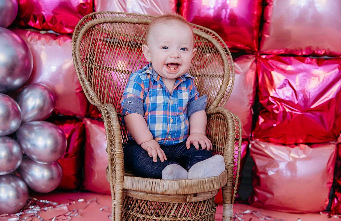 Ryler joined the competition — help win amazing prizes! baby, smiling, child, plaid_shirt, socks, wicker_chair, balloons, pink, silver, metallic, background, celebration, happy, portrait, indoor, cute, infant, festive, colorful, joyful