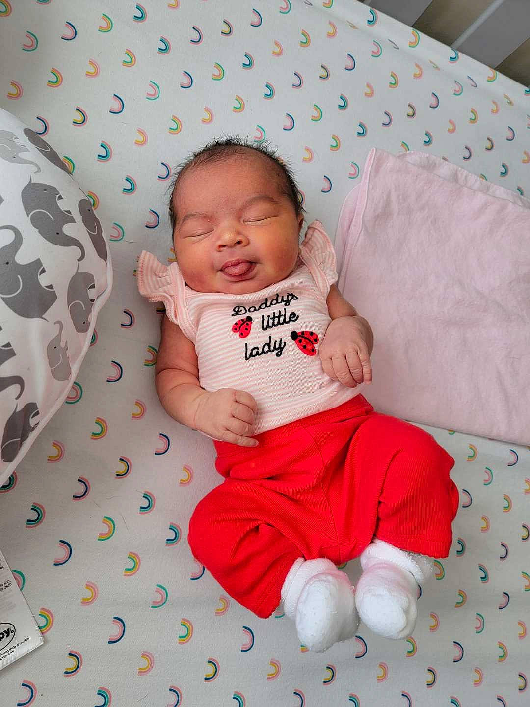 Emy is registered to the contest to win money with this photo: baby, baby_products, baby_toddler_clothing, bedding, cheek, child, comfort, event, finger, happy, linens, pattern, person, pink, product, room, sitting, skin, sleeve, textile