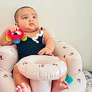 Durva is registered to the contest to win money with this photo: baby, infant, toy, rattle, inflatable_chair, child, sitting, cute, indoor, comfort, foot, hand, black_clothing, pattern, wall, face, expression, relaxing, skin, young