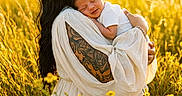 Aria joined the competition — help win amazing prizes! woman, baby, infant, field, yellow_flowers, tattoo, white_dress, sunlight, nature, outdoor, portrait, love, mother, child, peaceful, grass, warm_light, holding, smile, relaxation