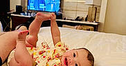 Keziah is registered to the contest to win money with this photo: baby, child, bed, smile, happy, indoor, person, television, furniture, lamp, blanket, clothing, feet, hand, head, room, wall, table, adult_hand, comfort