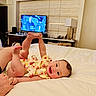 baby, child, bed, smile, happy, indoor, person, television, furniture, lamp, blanket, clothing, feet, hand, head, room, wall, table, adult_hand, comfort