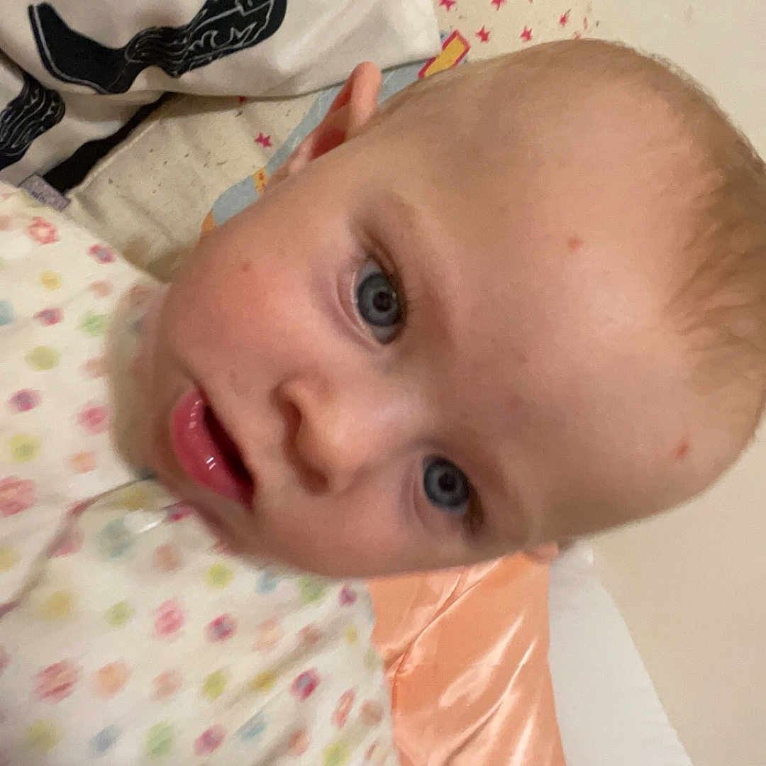 Aurora West is registered to the contest to win money with this photo: baby, bed, blanket, blue_eyes, child, closeup, cute, expression, face, head, indoor, infant, onesie, person, pillow, polka_dot, skin, sleepwear, star_pattern, young