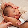 newborn, baby, sleeping, hands, adult_hands, cradling, close_up, skin, infant, peaceful, beige, soft_lighting, portrait, family, tenderness, comfort, clothing, bed, resting, caring