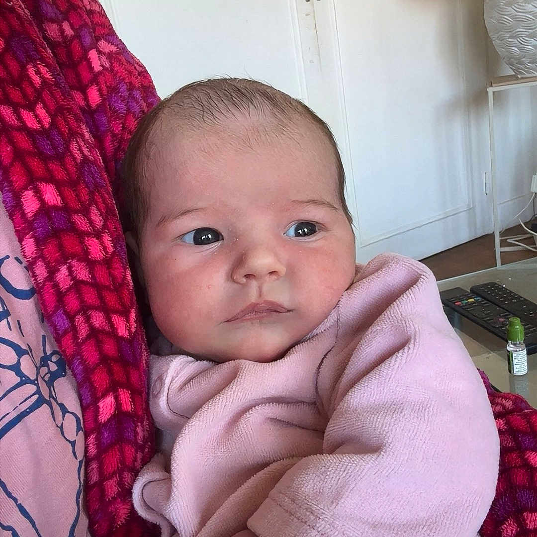 Lilyana a rejoint le concours — aidez-le/la à gagner de superbes lots ! baby, casual, child, cozy, curious, face, furniture, hand, holding, home, indoor, infant, lamp, patterned_skirt, person, pink_clothing, portrait, remote_control, soft_texture, table