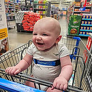 Jameson is registered to the contest to win money with this photo: baby, shopping_cart, walmart, smiling, child, grocery_store, aisle, clothing, happy, infant, retail, store, person, retail_environment, shopping, cute, holding, metal, plastic, indoor