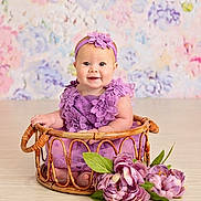 Kensley is registered to the contest to win money with this photo: baby, child, purple_dress, headband, smiling, wicker_basket, flowers, floral_background, indoor, cute, portrait, sitting, decor, head, skin, happy, infant, person, floor, hands