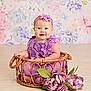 baby, child, purple_dress, headband, smiling, wicker_basket, flowers, floral_background, indoor, cute, portrait, sitting, decor, head, skin, happy, infant, person, floor, hands