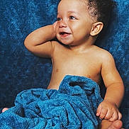 Vincent is registered to the contest to win money with this photo: baby, child, smile, curly_hair, blue_blanket, soft_texture, happy, portrait, infant, bare_chest, cute, relaxed, cozy, indoors, skin, hand, foot, face, expression, photography