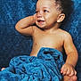 baby, child, smile, curly_hair, blue_blanket, soft_texture, happy, portrait, infant, bare_chest, cute, relaxed, cozy, indoors, skin, hand, foot, face, expression, photography