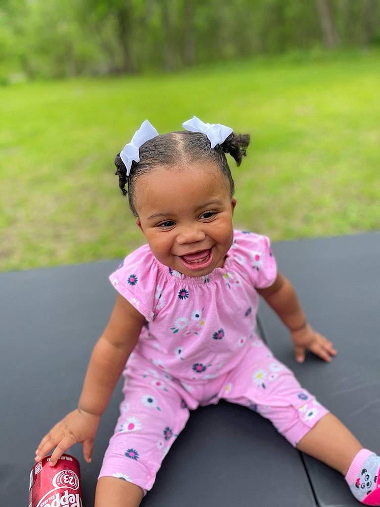 Leasia is registered to the contest to win money with this photo: baby_toddler_clothing, child, facial_expression, fashion_accessory, fun, grass, happy, joy, leisure, magenta, person, pink, recreation, shorts, sitting, skin, sleeve, smile, t_shirt, thigh